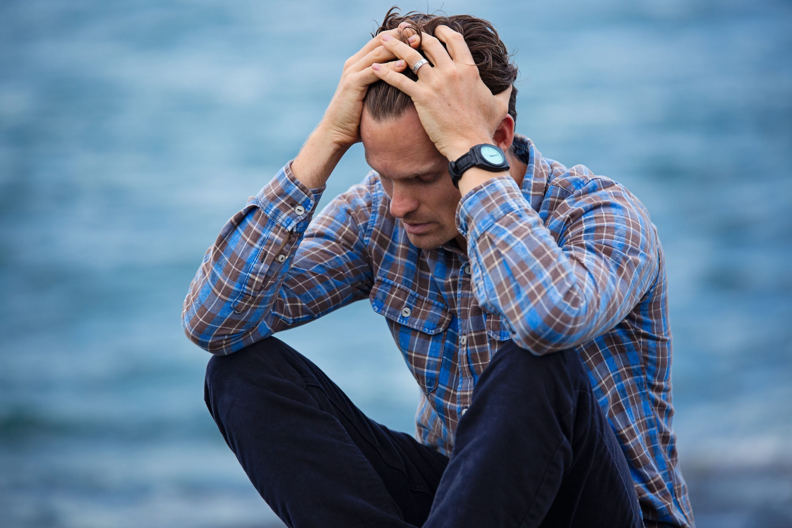 Man wearing blue plaid with hands in hair in distressed or sad pose