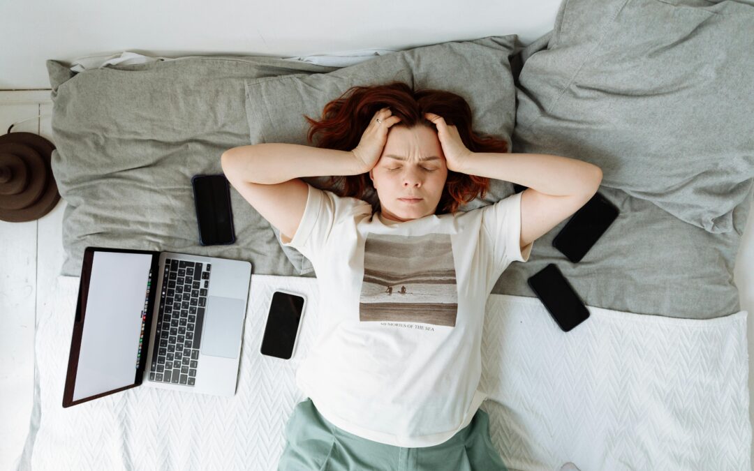 A Stressed Woman Lying on a Bed beside Cellphones and a Laptop