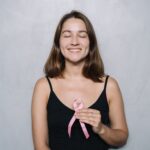 A smiling woman with eyes closed holds a pink breast cancer awareness ribbon, symbolizing hope and health